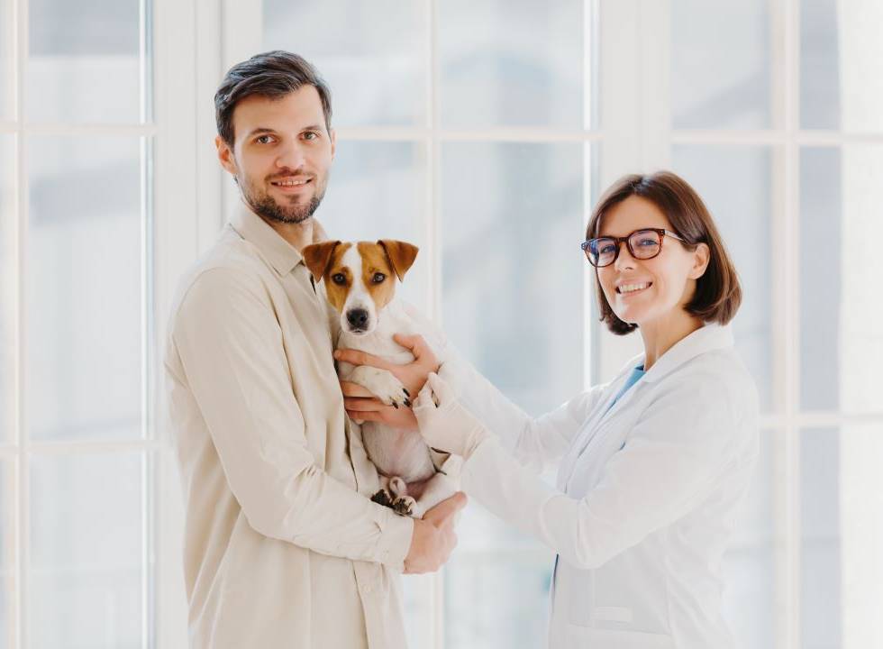 Man holding a small dog while a smiling female veterinarian in a white coat gently examines the pet.