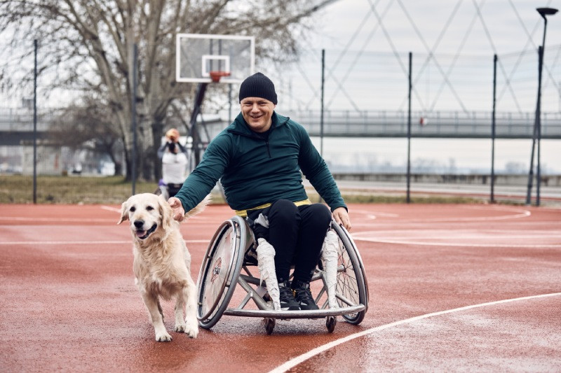 Man in a wheelchair and his dog on a basketball court.